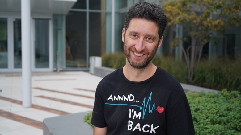 A man smiling at the camera wearing a shirt with a heartbeat that reads, 