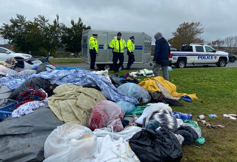 Police standing near a lot of wet debris, like blankets and clothing. Police near a trailer in the background