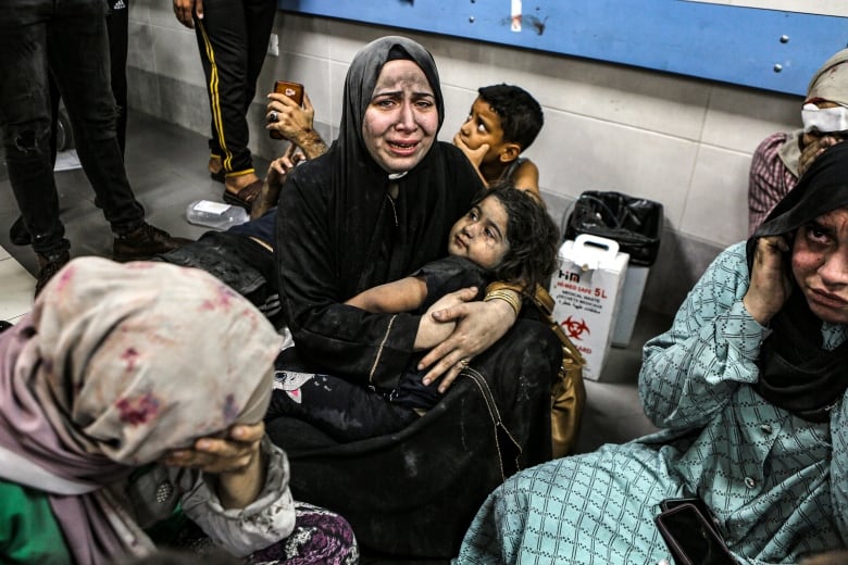 Crying, a woman holds her child on the floor, surrounded by others at al-Shifa hospital, following Israeli airstrikes in Gaza City.