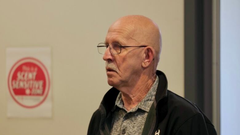 Man in glasses and black jacket stands next to 