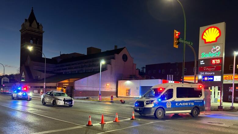 Police vehicles are seen along a stretch of a city road, next to a gas station.