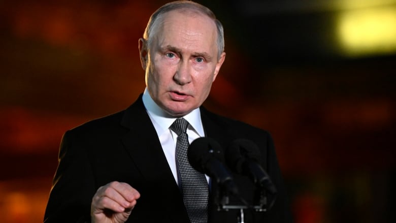 A man in a dark suit speaks at a podium.