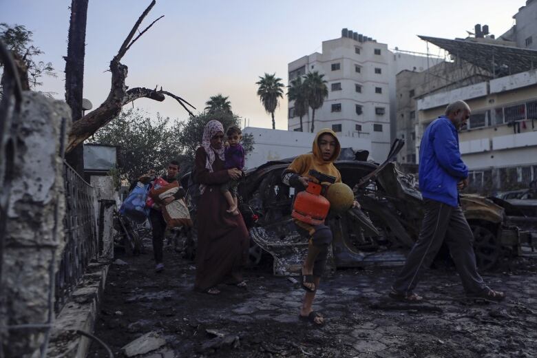 Families in Gaza carry belongings as they leave the ruins of a hospital hit by an airstrike.