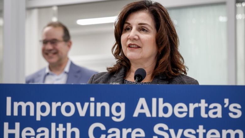 A woman is pictured behind a sign that reads 'Improving Alberta's Health Care System.'