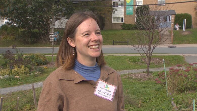 A woman stands smiling in a green space next to a road.