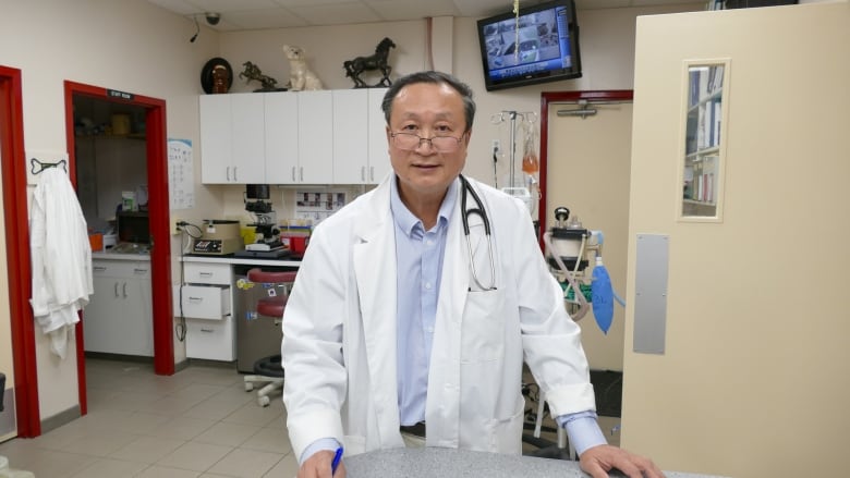 A veterinarian wearing a white coat with a stethoscope around his shoulders is standing in his veterinary practice.