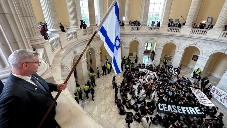 Man holds Israeli flag on second floor, above crowd of protesters on first floor of U.S. Capitol