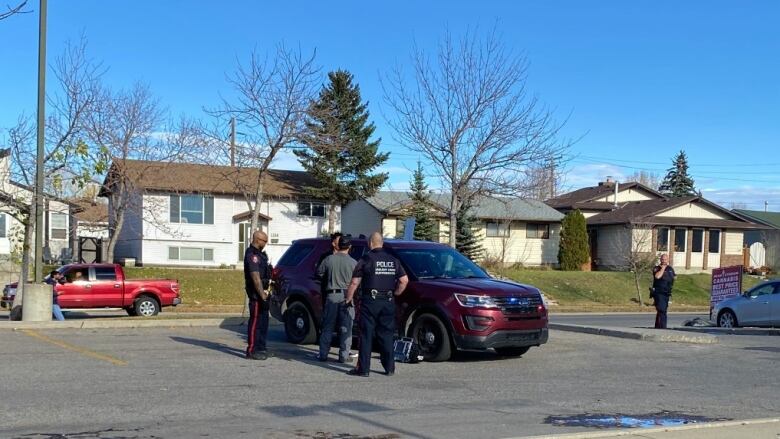 Police stand around a red car in a parking lot.