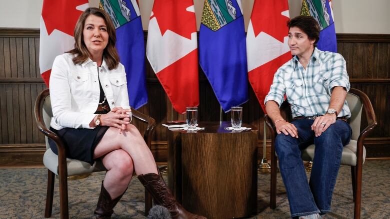 A male politician looks as a woman counterpart speaks. Both are seated and wearing western costumes.