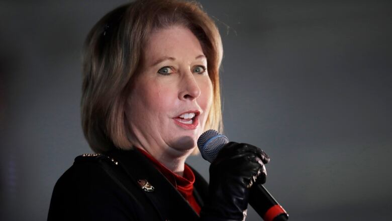 A woman with her below her chin holds a microphone with a gloved hand.