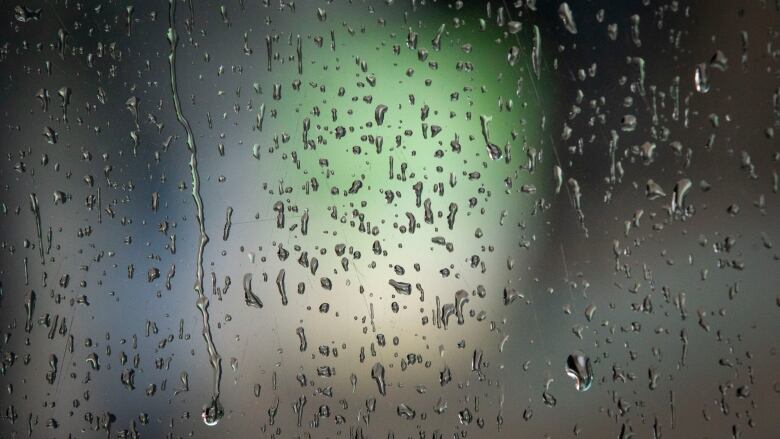 Raindrops are shown in closeup on a pane of glass.