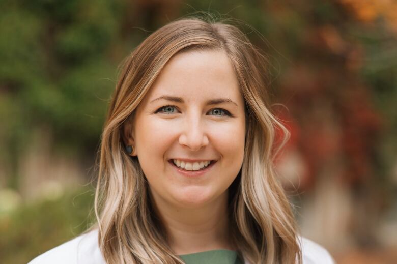 A blonde woman with a white lab coat smiles for the camera.