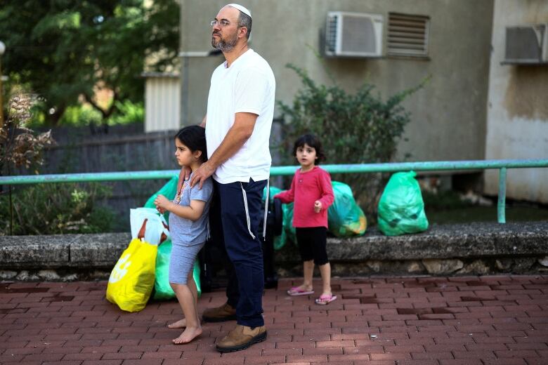 A man wearing a Jewish headcap is shown with two small children standing on a sidewalk.