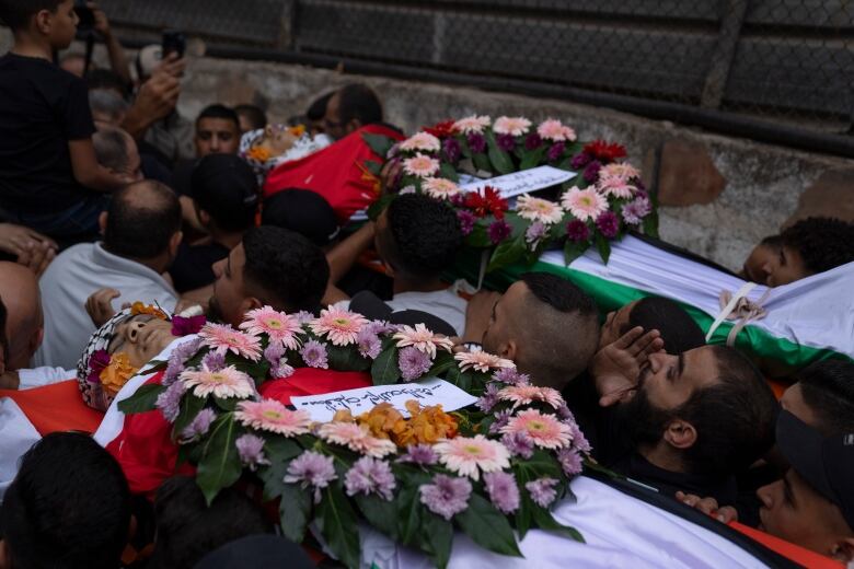 Two coffins covered with floral arrangements are lifted on the shoulders of several men.