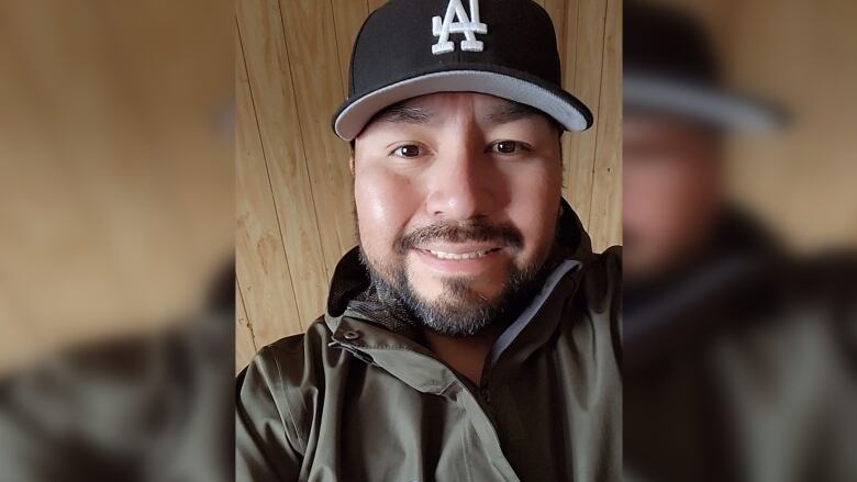 A man with dark hair wears a baseball cap with the LA logo. He smiles at the camera