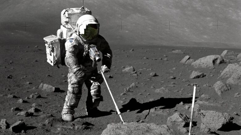 Astronaut Harrison Schmitt is seen on the surface of the moon with a long pole outstretched to a large boulder.