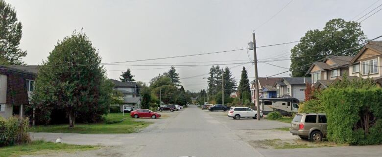 A suburban street with cars parked in front of single detached houses.