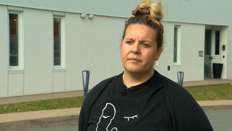 A woman in a black sweater stands in front of a building. 