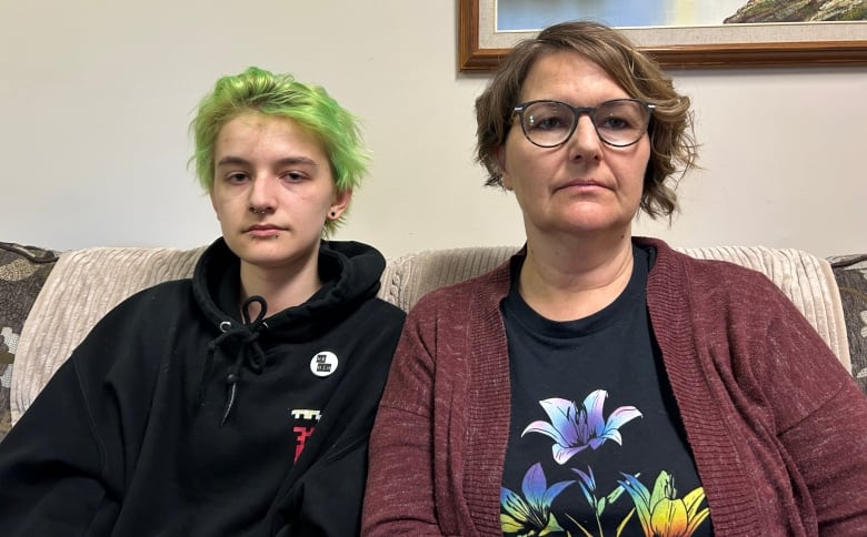 A teenage boy with green hair sits on a couch next to a woman in a red sweater.