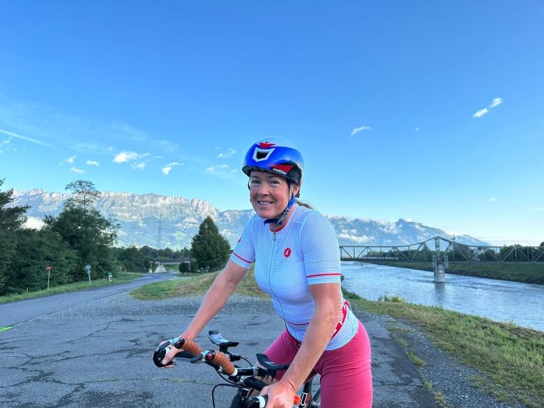 Woman in gear riding a bicycle with mountains and river in the background