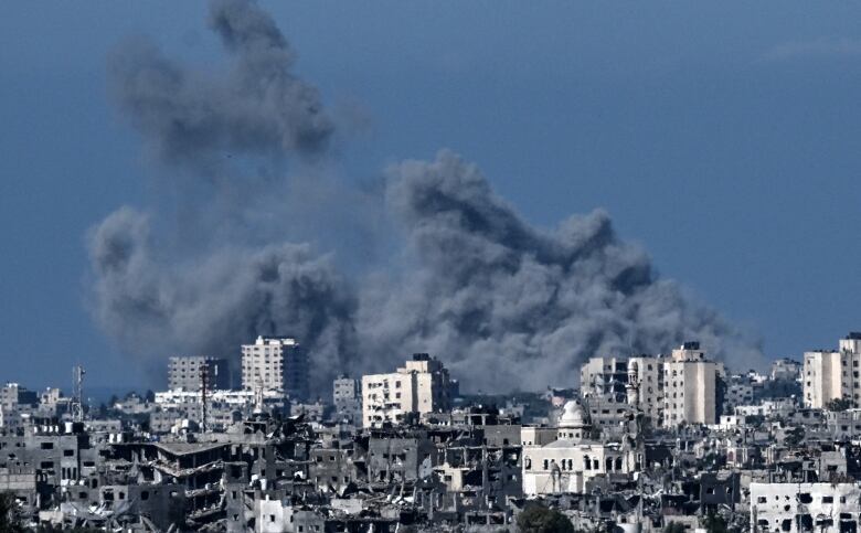 Large, dark grey clouds rise into the blue sky above damaged concrete buildings. 