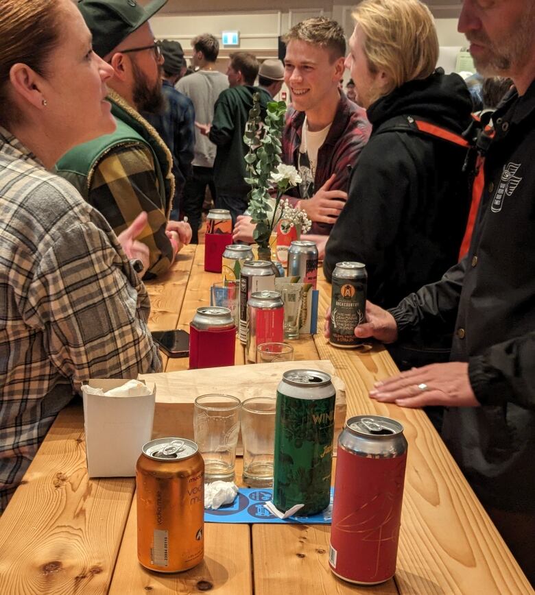 People stand and talk at a high table covered in glasses and beer cans