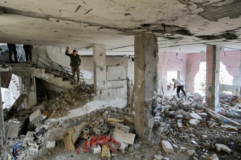 A man stands on stairs inside a damaged concrete building with piles of concrete blocks  and debris piled around the floor.