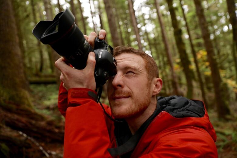 A man wearing a red jacket takes a picture in a giant forest.