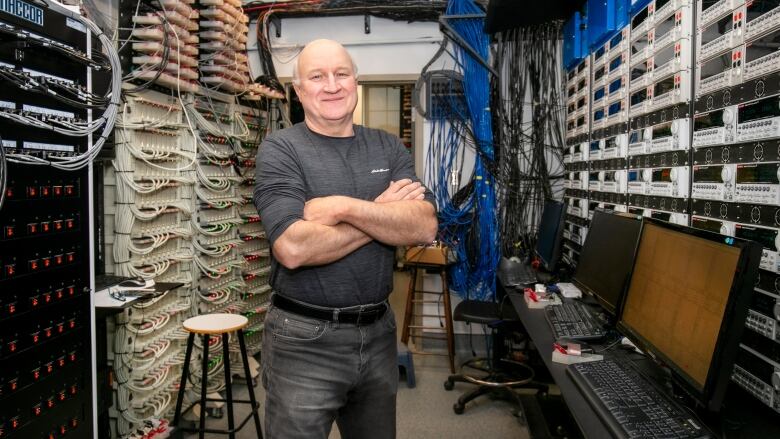 Man in a black sweatshirt poses in front of a bank of electrical components.