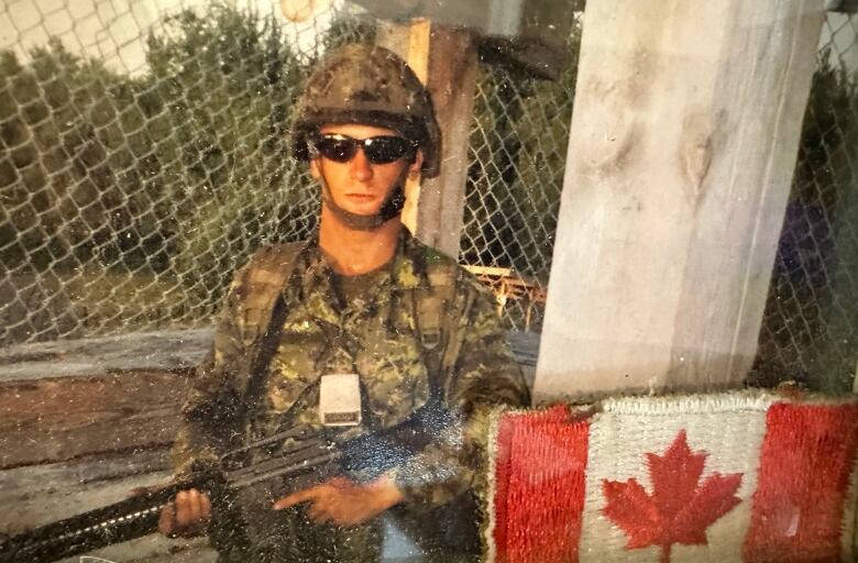 A soldier poses with his rifle in a framed photograph decorated with a Canadian flag patch.