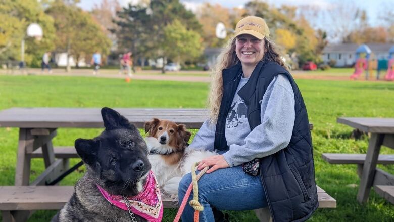 A woman sits at a picnic table with two dogs 