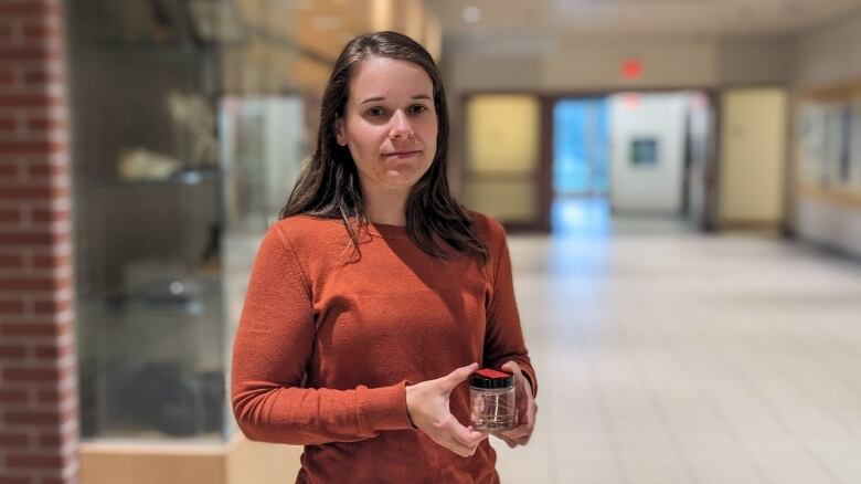 A woman standing in a hallway holding a sample jar 