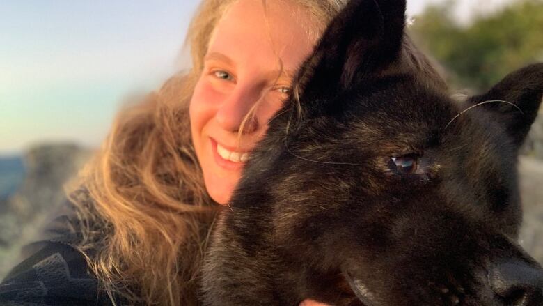 A woman with blonde hair hugs a black dog 