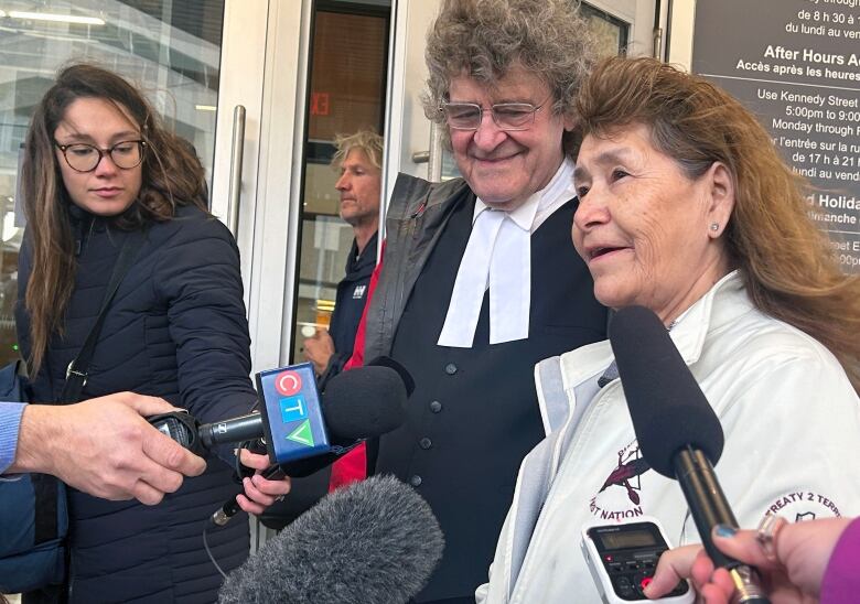 A woman with long hair speaks to several reporters. 