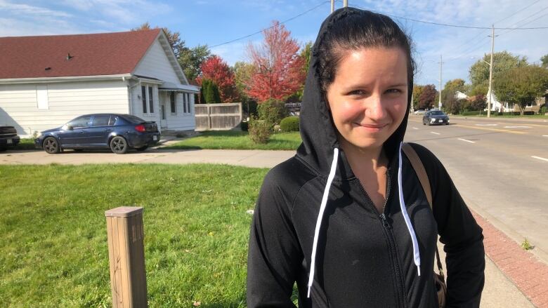 A woman wearing a black hoodie standing next to a road