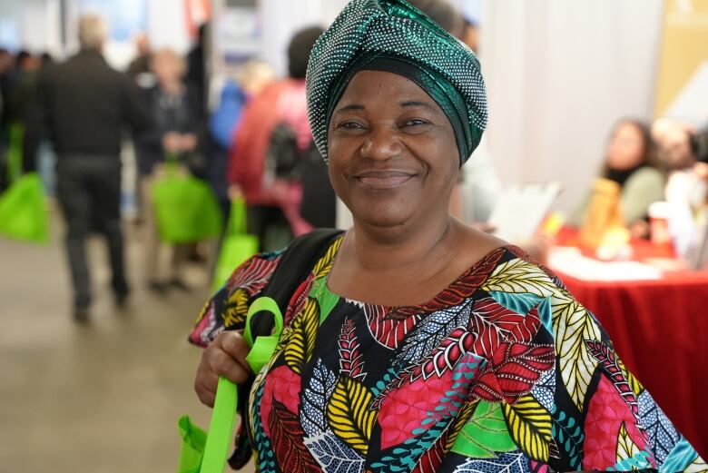 A woman with a green headwrap and multicolor shirt smiles.