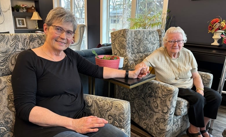 Woman in black shirt holds elderly woman with white hair's hand.