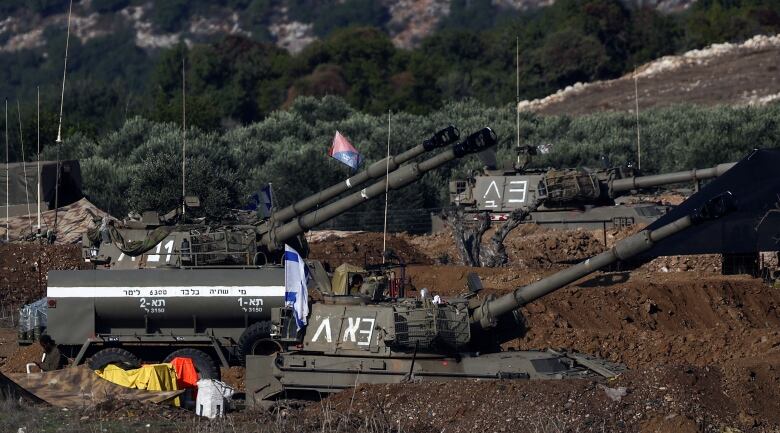 Three tanks, their guns angled up, sit amid some mounds of earth and scrub vegetation.