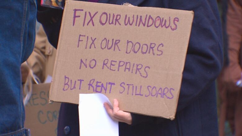 A sign that reads 'Fix our windows, fix our doors, no repairs, but rent still soars'.