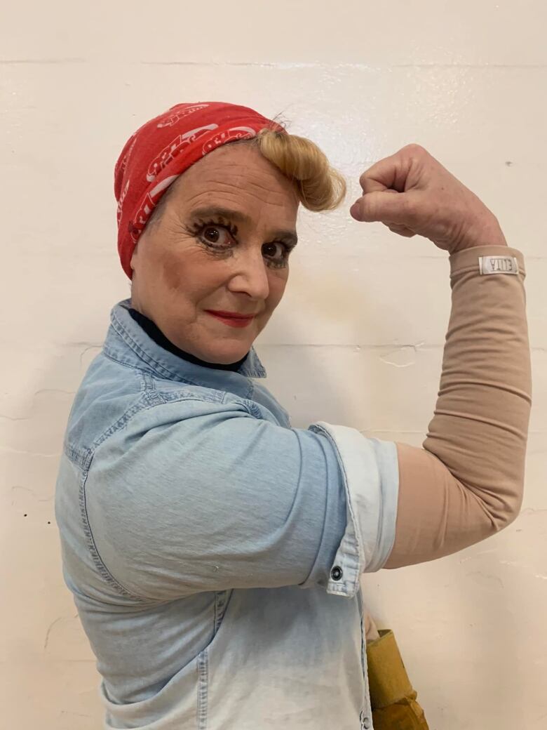 A woman wearing a red bandanna and full sleeves flexes her muscles.