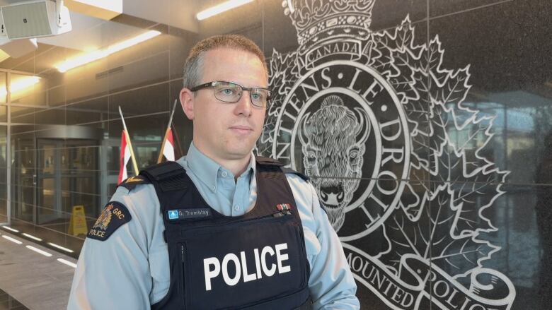 An RCMP officer is shown in uniform wearing a blue vest over a light blue shirt with the words 'police' in white writing on the front.