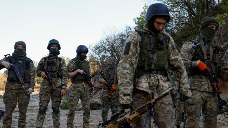 Soldiers in green camouflage uniforms walk down a dirt road.