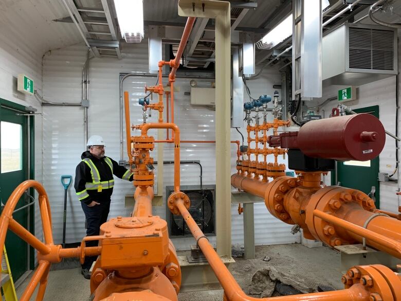 A man in a safety vest stands inside a room with various valves and monitors.