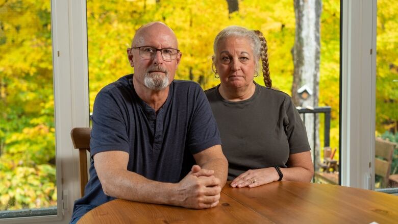 An older couple sits at a table with fall leaves visible through the window behind them.