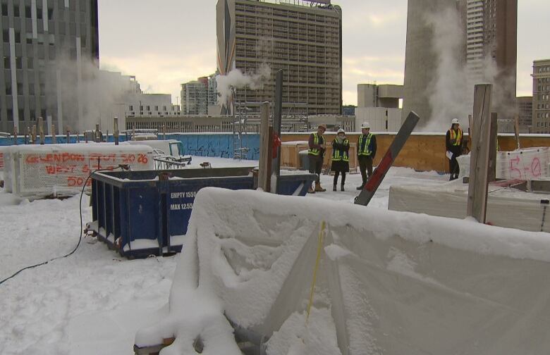 Several people in construction vests stand on a snow-covered rooftop.