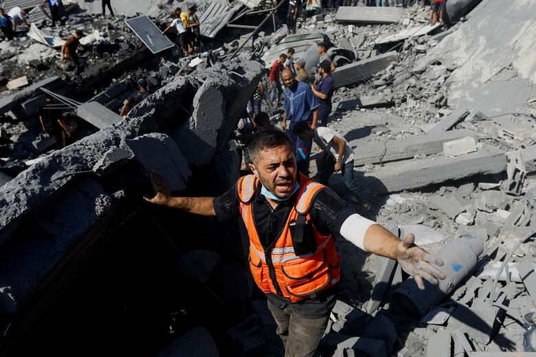 A man in a bright orange vest climbs over rubble searching for survivors after an air strike hit a concrete building.