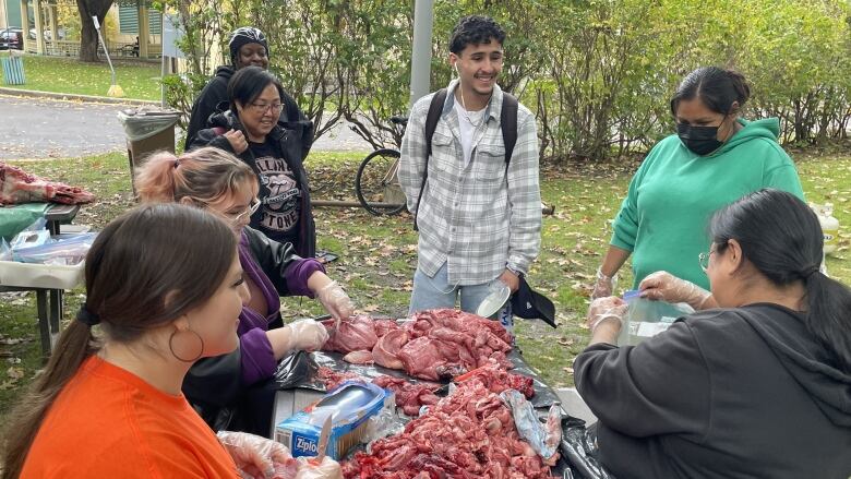 A group of students butchering moose meat on a wooden table outside. 