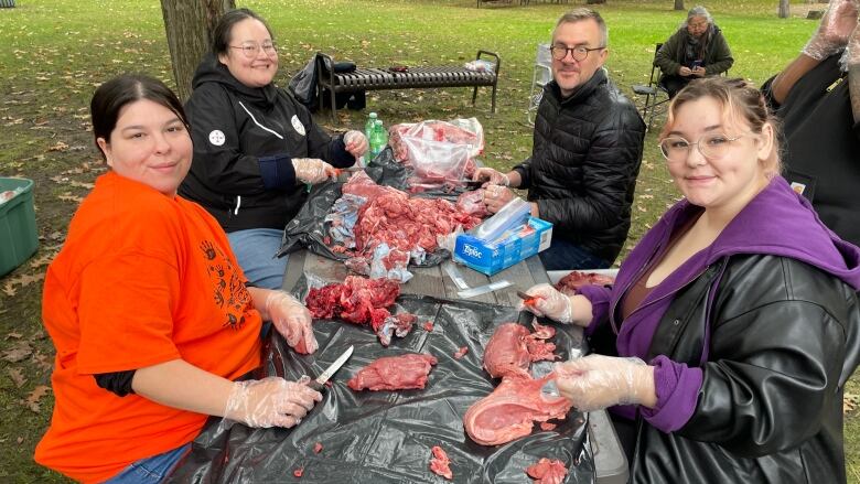 A group of students and professors cut moose meat together.