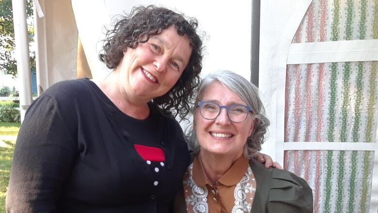 Two women sit close to each other and smile at the camera.