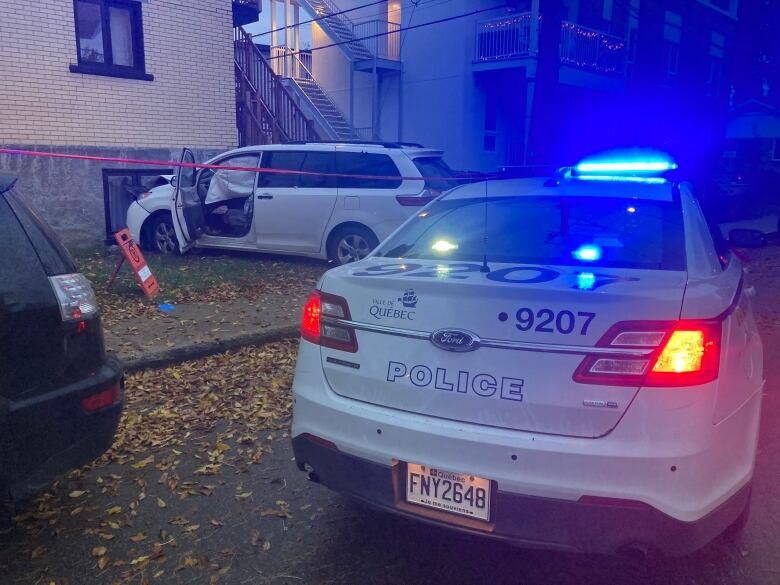 A wrecked car behind police tape, near a police cruiser. 